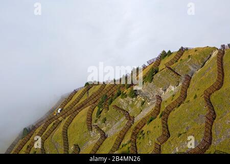 Obstacles aux avalanches sur la pente du sommet du Maennlichen près de Wengen. Vue sur la vallée de Lauterbrunnen sous une couverture de brouillard. Banque D'Images