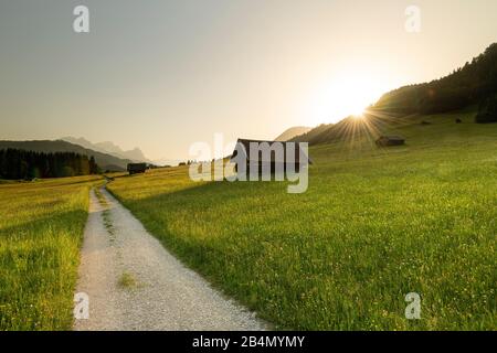 Coucher de soleil avec haystacks et route de terre, en arrière-plan le Zugspitze sur le Geroldsee Banque D'Images