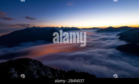 Les lumières de Maurach et de Pertisau sur le lac Achensee brillent sous la mer des nuages du brouillard élevé qui monte pendant une exposition de nuit à long terme. En arrière-plan, les montagnes de Karwendel, prises de l'Ebener Joch dans le Rofan. Banque D'Images