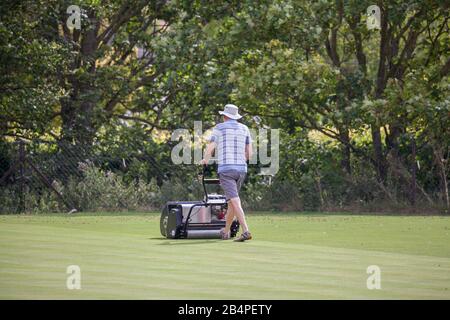 Homme fauchant la pelouse à un vert de bowling Banque D'Images