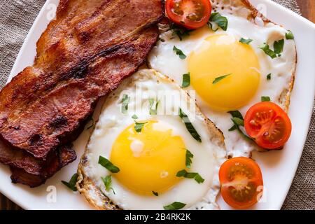 œufs frits bacon frit et tomates cerises sur une plaque blanche saupoudrée de persil Banque D'Images