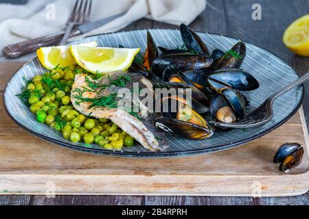 Bar de mer avec petits pois, moules et citron garnis de l'aneth frais Banque D'Images