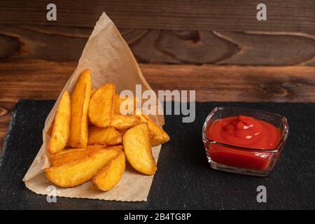 Pommes de terre rustiques avec vaisselle en ketchup ardoise, pierre noire sur fond en bois. Gros plan. Banque D'Images