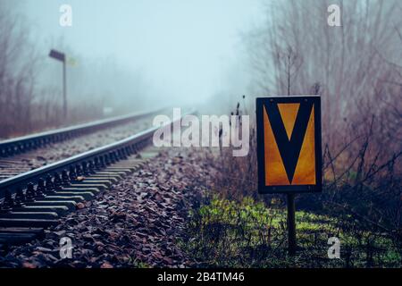 Signe ferroviaire signifiant début de la limite de vitesse s'étire au remblai de chemin de fer avec la voie ferroviaire disparaissant en brouillard en arrière-plan Banque D'Images