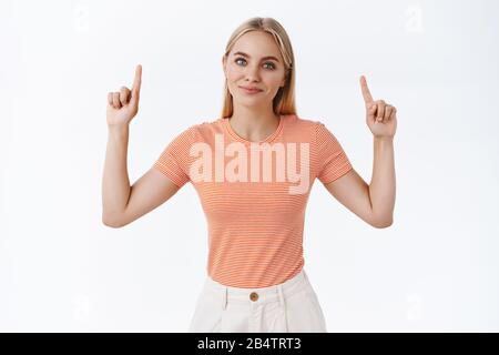 Jolie fille moderne et sassy de style de vie de femme blogger, blonde tatouée fille dans un t-shirt rayé, levant les mains pointant vers le haut et sourire comme suggérant essayer nouveau Banque D'Images