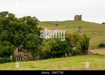 Chapelle St Catherine à Abbotsbury perchée sur une colline avec une vieille maison en pierre nichée parmi les arbres au premier plan à Dorset, en Angleterre. Banque D'Images