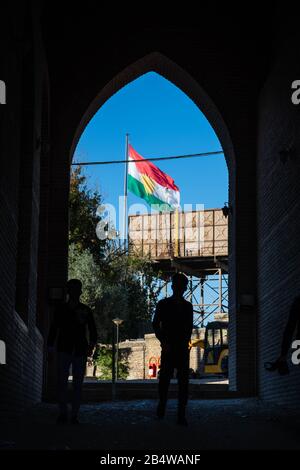 Irak, Kurdistan irakien, Arbil, Erbil. Vue de dessous l'arche marquant l'entrée de la citadelle de Qalat. En arrière-plan un drapeau kurde. Trois jeunes Banque D'Images