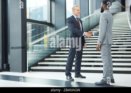 Prise de vue horizontale complète de deux hommes ayant réussi à la diversité ethnique qui se secouent les mains Banque D'Images
