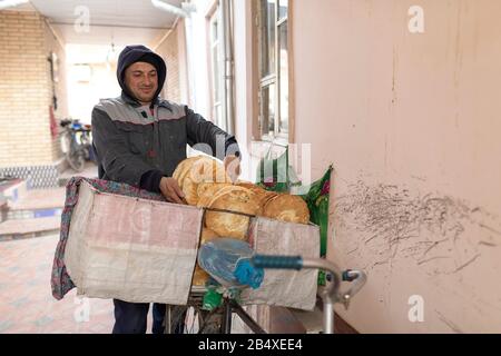 Vendeur de pain transportant du pain typique à vélo de la boulangerie dans la vieille ville de Boukhara, Ouzbékistan Banque D'Images