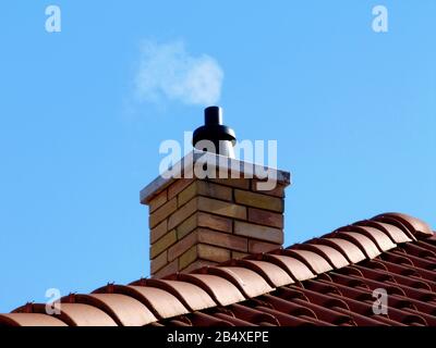 cheminée en brique. pierres de plafond en béton. carreaux de toiture en argile stack.brown en céramique grise avec éléments de crête incurvés. ciel bleu. fumée blanche. vue à faible angle Banque D'Images