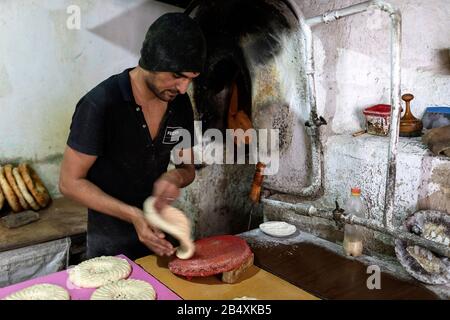 Homme préparant du pain ouzbek traditionnel dans une petite boulangerie à Boukhara, en Ouzbékistan Banque D'Images