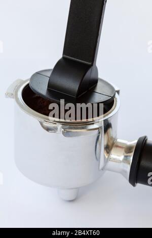 Tassage du café moulu dans un porte-filtre pour machine à espresso domestique avec une autosurveillance en plastique sur fond Uni Banque D'Images