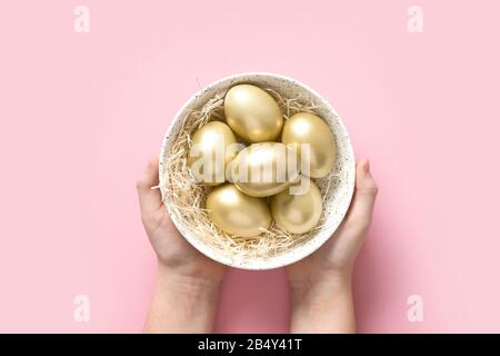 Oeufs de poulet dorés de Pâques dans les mains des enfants sur fond rose. Vue de dessus. Gros plan. Banque D'Images