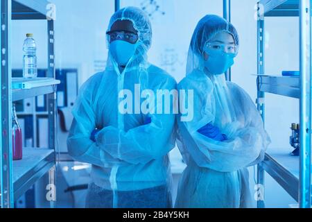 Portrait horizontal moyen de deux scientifiques de laboratoire non reconnaissables en tenue de travail protectrice debout avec des bras croisés regardant la caméra Banque D'Images