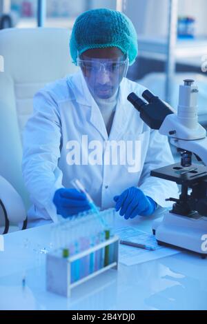 Tir vertical à grand angle de jeune homme africain américain portant un manteau blanc travaillant dans le laboratoire de recherche médicale moderne ivestigating et développement ne Banque D'Images