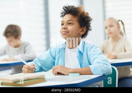 Trait horizontal du jeune garçon africain américain assis à la réception de l'école écoutant attentivement son professeur, copier l'espace Banque D'Images