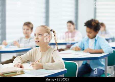 Petite fille curieuse avec cheveux blonds assis à la réception de l'école à l'écoute de son professeur, portrait horizontal, espace de copie Banque D'Images