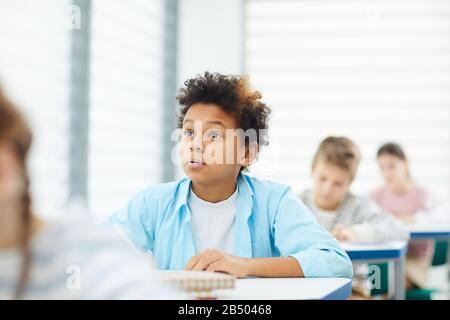 Curieux jeune garçon avec les yeux large ouvert assis à la réception de l'école à l'écoute de son enseignant, portrait horizontal, espace de copie Banque D'Images