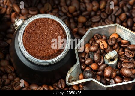 Gros plan d'une cafetière italienne ouverte avec café moulu dans le filtre métallique, sur de nombreux grains de café torréfiés Banque D'Images