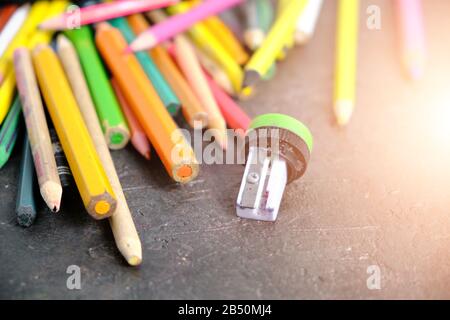 Vieux crayons de couleur dispersés sur le sol et un aiguiseur cassé dans la lumière du soleil Banque D'Images