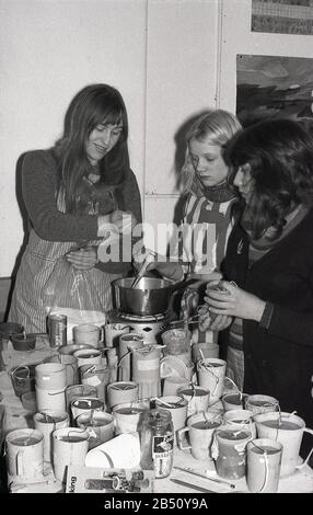 Années 1970, historique, jeunes femmes fabriquant des bougies, en utilisant un kit de fabrication de bougies DIY, avec un pot verseur et une plaque chauffante électrique de fonte de cire, Angleterre, Royaume-Uni. Banque D'Images