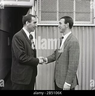 1960s, historique, entraîneur de football du Charlton Athletic FC, Bob Stokoe accueille un nouveau joueur au club, Charlton, Londres Sud, Angleterre, Royaume-Uni. Debout à l'extérieur de l'entrée, un hangar en métal ondulé, les deux hommes portent des vestes de sport à carreaux et chemise et cravates. Bob Stokoe était le Manager du club entre 1965 et 1967. Stokoe était célèbre pour sa victoire en FA Cup avec Sunderland, ainsi que pour être membre de l'équipe Newcastle FC qui a remporté la célèbre coupe dans les années 1950 Banque D'Images