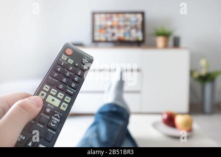 Homme regardant la télévision, allongé sur le canapé, jambes sur la table. Personne tenant la télécommande dans le salon Banque D'Images