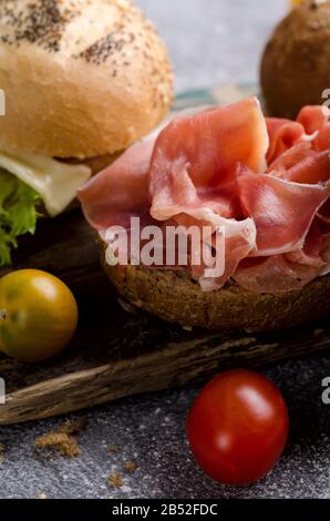 Délicieux pain hamburger croustillant avec jambon en tranches sur une planche à découper en bois d'époque. Sombre photo de nourriture moody bon pour le menu de bar et des affiches. Banque D'Images