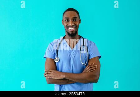 Portrait d'un médecin ou d'une infirmière sympathique portant un uniforme de gommage bleu et un stéthoscope, avec des bras croisés, isolés sur fond bleu de studio Banque D'Images