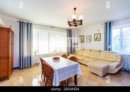 Grande salle lumineuse Sunny dans la maison. Au centre de la chambre se trouve une table avec une nappe blanche et quatre chaises en osier. Canapé en cuir blanc. Vintage Banque D'Images