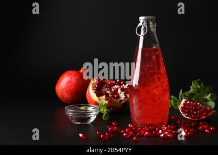 Boisson de grenade à la mode avec des graines de basilic en bouteille sur fond noir, gros plan Banque D'Images
