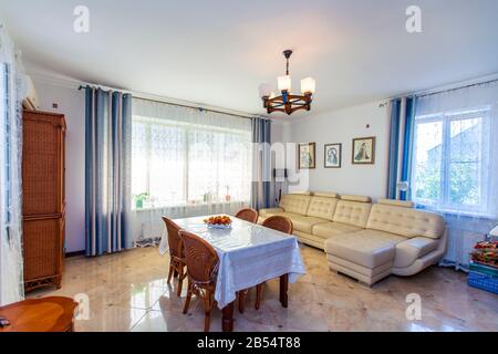 Grande salle lumineuse Sunny dans la maison. Au centre de la chambre se trouve une table avec une nappe blanche et quatre chaises en osier. Canapé en cuir blanc. Vintage Banque D'Images