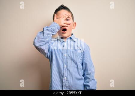 Jeune garçon enfant portant une élégante chemise debout sur un fond isolé peeking dans le revêtement de choc visage et les yeux avec la main, regardant par le doigt Banque D'Images