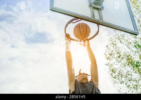 Jeune joueur de basket-ball rasta dunking dans le camp de ville de grunge urbain avec le soleil arrière extérieur - sportif athlète exécutant slam dunk sur le terrain - Sp Banque D'Images