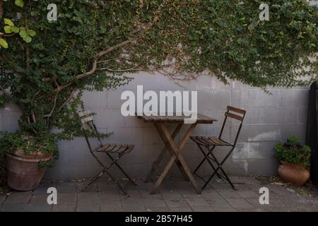 Place extérieure dans un café avec une table en bois vide et deux chaises vides et de l'ivy croissant sur le mur derrière. Banque D'Images