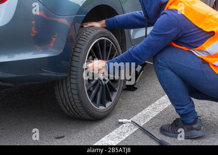 Un homme dans un gilet de sécurité orange change un pneu plat sur une route. Gros plan se rapproche de la roue d'une voiture cassée. Remplacement d'une roue à l'aide de Banque D'Images