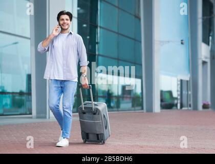 Homme Marchant Avec Suitcase À L'Extérieur De L'Aéroport Et Parler Sur Cellphone Banque D'Images