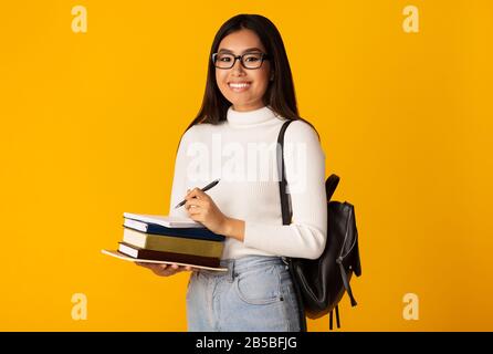 Asian Student Girl Holding Books Debout Sur Fond Jaune, Studio Banque D'Images