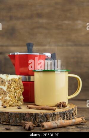 Une tasse de café chaud en étain jaune avec une cafetière italienne (Moka) et un gâteau sur une table en bois. Banque D'Images