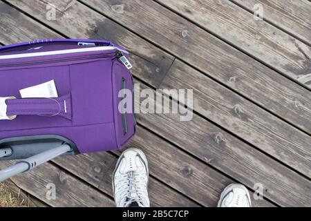 Concept de voyage. Photo du niveau des yeux. Vue sur les jambes et une valise pour le tourisme. Copier l'espace sur la texture du bois Banque D'Images