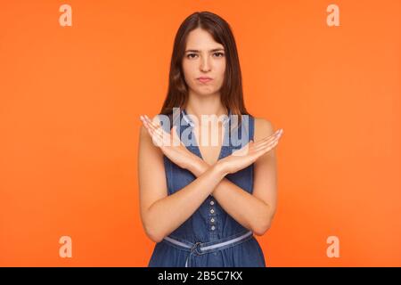 Pas de moyen, concept de refus. Une femme brunette agacée qui croise les mains dans le signe x et regarde insatisfaite, c'est-à-dire arrêter, montrant le no définitif, c'est fini. Banque D'Images