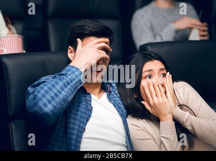 Jeune homme avec sa petite amie qui fermait des visages dans la terreur tout en regardant un film d'horreur au cinéma Banque D'Images