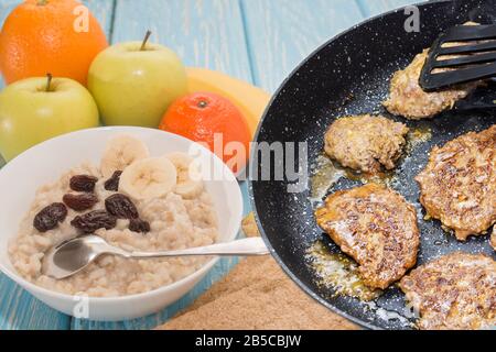 Petit déjeuner sain et malsain. Flocons d'avoine avec raisins secs dans un bol blanc. Fruits. Steaks frits. Banque D'Images