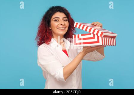 En prévision de la surprise. Portrait d'une jolie femme hipster avec des cheveux rouges fantaisie tenant ouvert boîte cadeau et sourire à l'appareil photo, satisfait de bi Banque D'Images