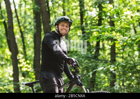 Jeune cycliste sportif souriant à l'appareil photo, forêt verte Banque D'Images