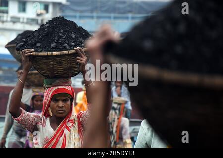 La femme ouvrier porte un panier rempli de charbon sur sa tête dans la région de Gabtoli à Dhaka, au Bangladesh, le mars 2020. Banque D'Images