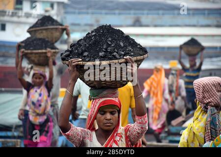 La femme ouvrier porte un panier rempli de charbon sur sa tête dans la région de Gabtoli à Dhaka, au Bangladesh, le mars 2020. Banque D'Images