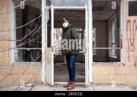 jeune homme dans un masque médical debout à l'entrée d'un bâtiment hospitalier abandonné. abri épidémique. Banque D'Images