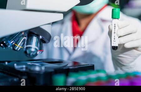 Microbiologiste avec un tube d'échantillon biologique contaminé par le coronavirus avec l'étiquette Covid-19 / médecin en laboratoire avec un tube biologique pour Banque D'Images