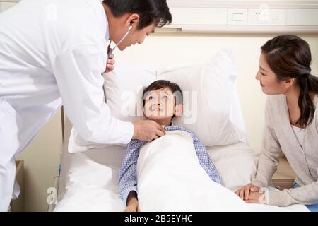 Cinq ans asian kid Lying in Bed in hospital ward accompagnée de mère et d'être examiné par le pédiatre en utilisant stethoscope Banque D'Images